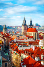 High Spires Towers Of Tyn Church In Prague City (Church Of Our Lady Before Tyn Cathedral) Urban Landscape Panorama With Red Roofs Of Houses In Old Town And Blue Sky With Clouds