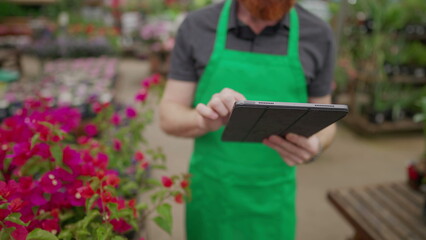 Wall Mural - Close-up of staff_s hand holding tablet browsing inventory inside local business. Young man wearing green apron using modern technology at Flower Shop