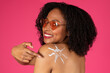 Leinwandbild Motiv Glad young black curly lady in sunglasses pointing finger at shoulder sunblock