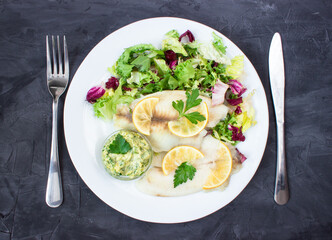 Wall Mural - steamed tilapia fish with salad and tartar sauce with appliances on dark background. vertical