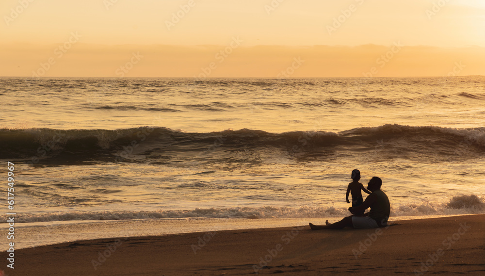 Padre e hijo sentados frente al mar a contraluz en un atardecer de ...