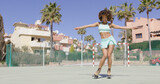 Young fit girl holding hands apart and dancing in roller skates on playground in sun light.
