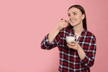 Wall Mural - Woman eating tasty yogurt on pink background, space for text