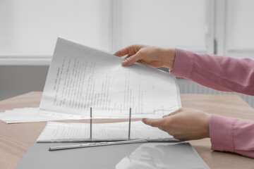 Wall Mural - Woman putting punched pocket with document into folder at wooden table, closeup