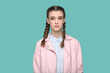 Portrait of serious strict young teenager girl with braids wearing pink jacket looking at camera with bossy expression, being in bad mood. Indoor studio shot isolated on green background.