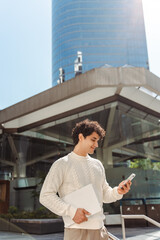 Relaxed young Latin American man using mobile phone, checking social media content, scrolling news feed, messaging, posting photos on his social account, ordering food, booking. People and technology