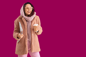 Poster - Stylish young woman in teddy coat with cup of coffee and newspaper on pink background