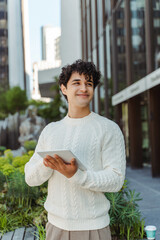 Portrait of smiling curly haired latin man holding digital tablet, communication online