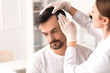© Pixel-Shot - Doctor examining young man's hair in clinic, closeup