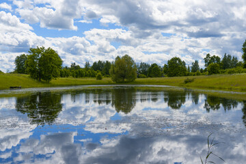 Canvas Print - Landscape blue lake, forest, green meadow and rain clouds in the distance