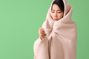 Ill Asian woman with plaid and thermometer on green background