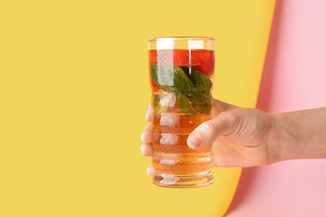 Wall Mural - Female hand holding glass of ice tea with strawberry and mint on colorful background