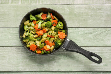 Wall Mural - Frying pan with tasty vegetables on green wooden background