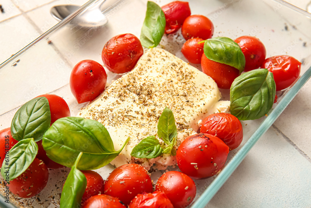Baking dish with tasty tomatoes and feta cheese on white tile background