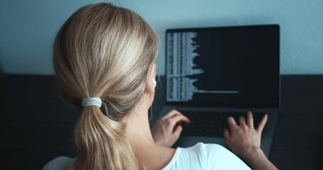 Rear view of woman programmer sitting in front of laptop computer monitor and coding. Close up back view of woman programmer working at computer, writes code at office workplace