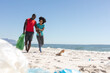 © wavebreak3 - Happy african american couple cleaning sunny beach and collecting litter, copy space
