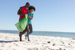 © wavebreak3 - Happy african american couple cleaning sunny beach and collecting litter, copy space