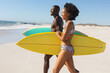 © wavebreak3 - Happy, fit african american couple carrying surfboards walking on sunny beach to the sea