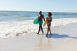 © wavebreak3 - Happy, fit african american couple carrying surfboards walking on sunny beach by the sea, copy space