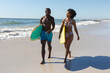 © wavebreak3 - Happy, fit african american couple carrying surfboards walking on sunny beach by the sea