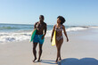 Happy, fit african american couple carrying surfboards walking on sunny beach by the sea