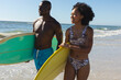 © wavebreak3 - Happy, fit african american couple carrying surfboards walking on sunny beach by the sea