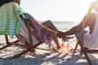 © wavebreak3 - Happy african american couple sitting in deckchairs holding hands on sunny beach by the sea