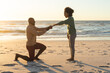 © wavebreak3 - Happy african american man kneeling and proposing to girlfriend on beach at sundown