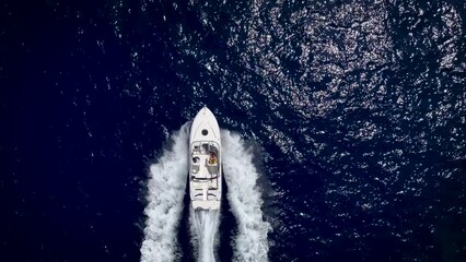 Wall Mural - high aerial top view of a motor yacht cruising with speed over blue, sparkling ocean and leaving a t