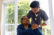 Happy diverse male doctor discussing with senior male patient in wheelchair at home