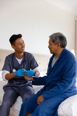 Happy diverse male doctor testing blood of senior male patient at home