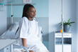 African american female patient sitting on bed and looking away in hospital room