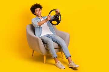 Canvas Print - Full length photo of cheerful satisfied man sitting in armchair hold steering wheel test new car isolated on yellow color background