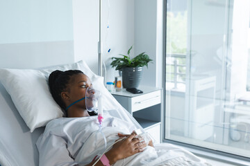 Wall Mural - African american female patient with oxygen mask, lying on bed in hospital room