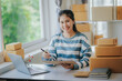 © Witoon - SME Entrepreneurs Small Business Entrepreneurs online sales concept Happy young smiling asian business owner working on computer and box at home. Delivery of SME parcel boxes, procurement, delivery to