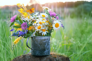 summer background. flowers in old metal cup close up on meadow, abstract natural background. useful 
