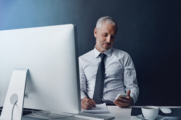 Canvas Print - Phone, computer and business man at desk online for social media, internet and browse website in office. Networking, corporate worker and mature male person on smartphone, writing notes and planning