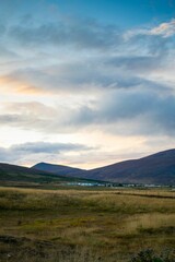 Poster - Scenic landscape of a rolling grassy field with a mountain range and fluffy clouds in the background