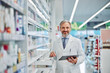 © bnenin - Portrait of a grey-bearded smiling male pharmacy employee with a tablet.