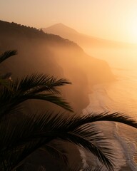 Wall Mural - Stunning sunset over a beach and majestic mountains with palm tree fronds visible in the foreground