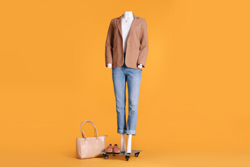 Wall Mural - Female mannequin with accessories dressed in white t-shirt, beige jacket and jeans on orange background. Stylish outfit