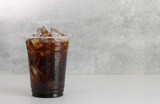 Ice americano coffee in a tall disposable glass over grey background on white table. Cold summer drink on dramatic grey background with copy space. 