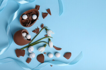 Wall Mural - Flat lay composition with tasty broken chocolate eggs and beautiful decor on light blue background. Space for text