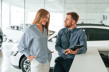 Information in the notepad. Man in formal clothes is with woman customer with the electric car