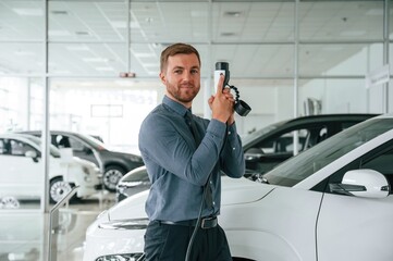 Having fun with charger. Handsome car dealership worker is with electric vehicle