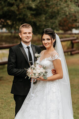 Wall Mural - portrait of the bride and groom in the park, the bride and groom look into the camera lens. Wedding walk in the park