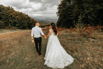 Wall Mural - Wedding couple walks in the mountains. The groom leads the bride by the hand. The dress of the bride develops in the wind.