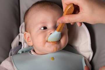 A mother feeds a 6-month-old caucasian baby fruit puree. First food for babies, close-up