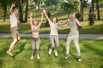 Wall Mural - Group of healthy runners team jumping in the air at city park during morning training.