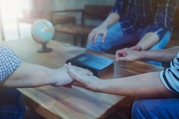 Wall Mural - Close up of a small group of christian friends holding hand and pray together wirh blur holy bible and world globe on wooden table, world missing concept